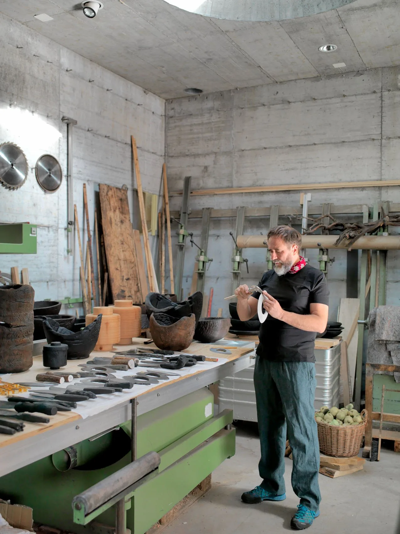 Othmar Prenner in his workshop, beside a table of black-burned wooden vessels and forged knives