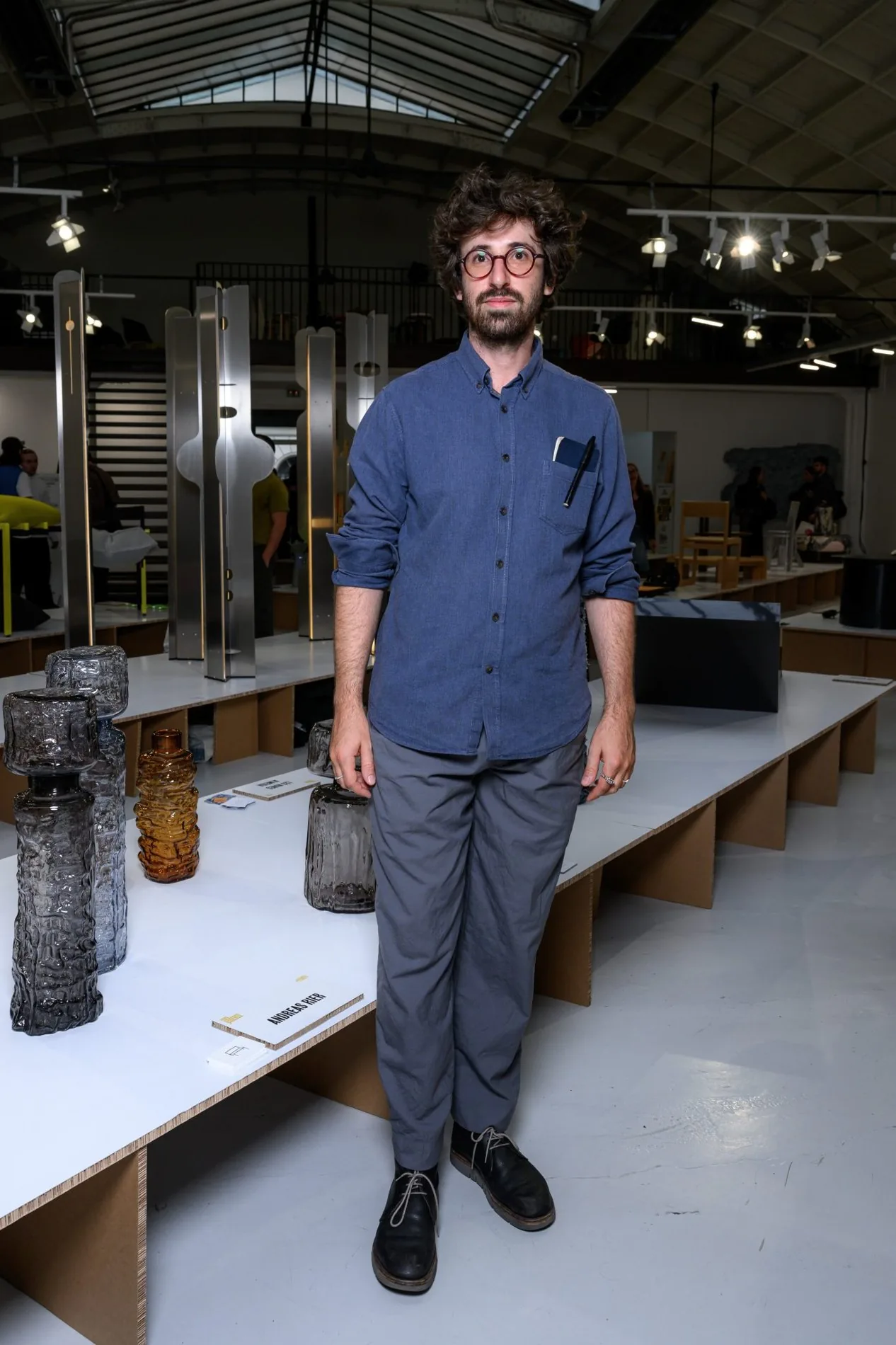 Andreas Rier standing beside his textured glass vessels at an exhibition