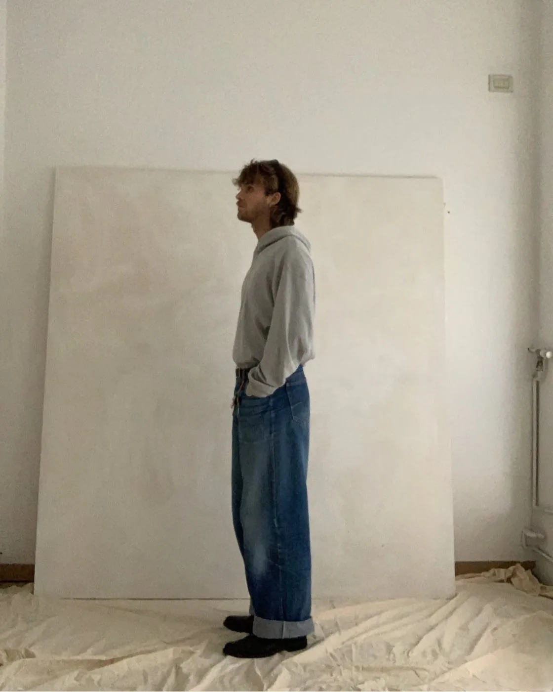 Alexander Koch standing in front of a large blank canvas in his studio